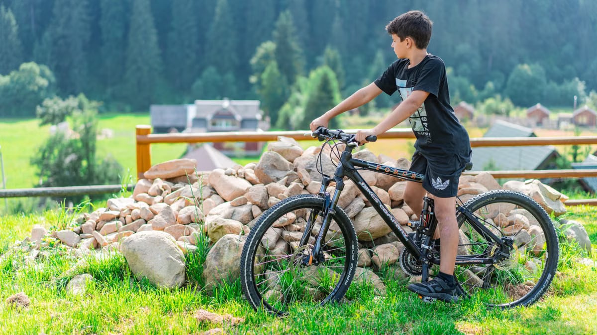A young boy rides a mountain bike in Bukovel, Ukraine with a scenic forest backdrop.