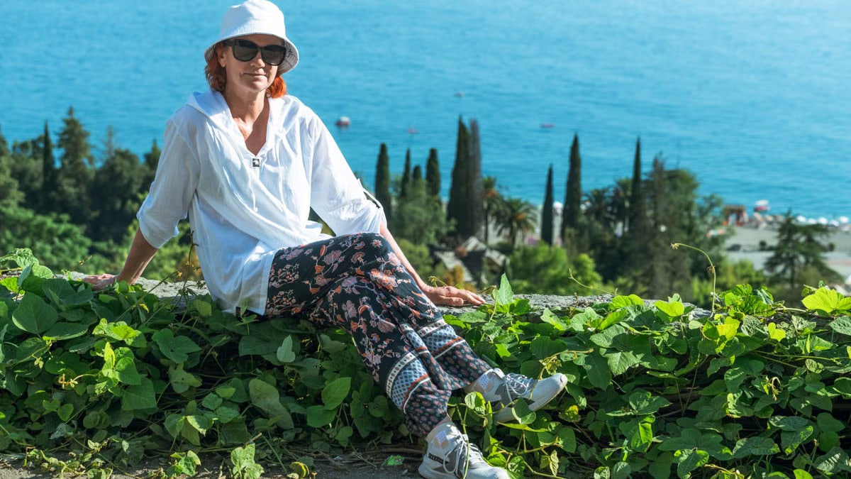 A woman enjoys a tranquil summer day by the sea, surrounded by lush greenery and a beautiful landscape.